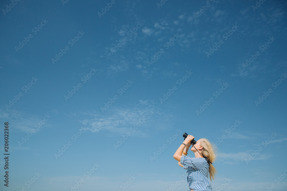 Beautiful natural blonde woman looking through binoculars against blue sky Beautiful natural blonde woman looking through binoculars against blue sky