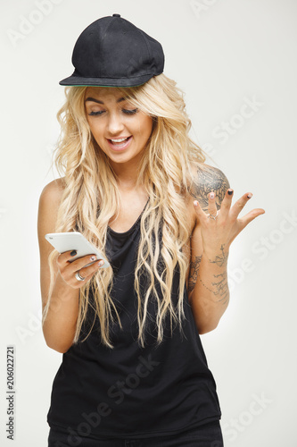 Stylish blonde looks at phone in surprise and spreads her hand in bewilderment over white isolated.