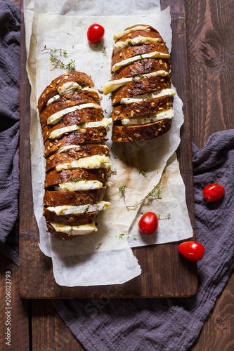 Hasselback baguette with camembert. Baked. Wooden table.
