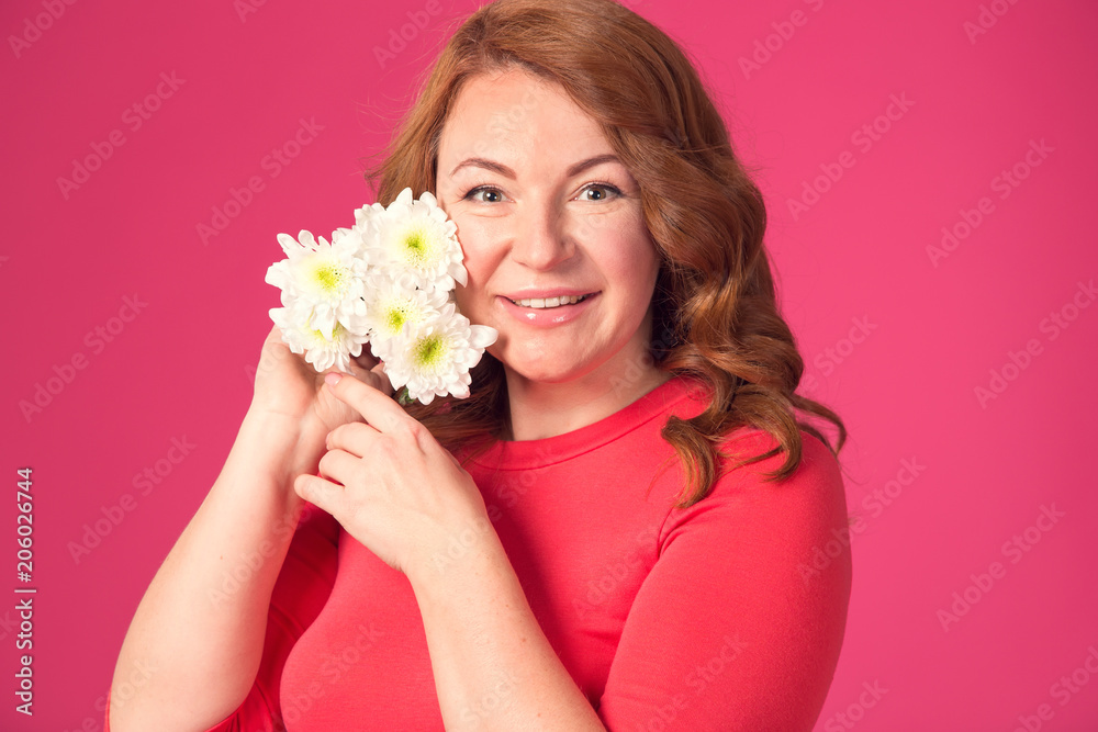 Beautiful red-haired woman with chrysanthemum flowers in hands on a pink background.