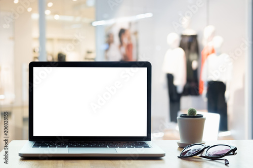 Laptop with blank screen on table. Clothes shop  blurred background.