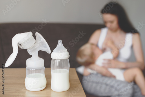 Bottle and breast pump with breast milk on the background of mother holding in her hands and breastfeeding baby. Maternity and baby care.