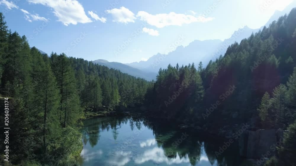 aerial forward over blue alpine lake revealing mountain forest valley in sunny summer with clouds.Europe Alps outdoors green nature scape mountains wild establisher.4k drone flight establishing shot
