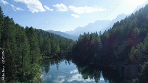 aerial forward over blue alpine lake revealing mountain forest valley in sunny summer with clouds.Europe Alps outdoors green nature scape mountains wild establisher.4k drone flight establishing shot