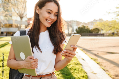 Happy woman walking in park looking aside chatting by mobile phone.