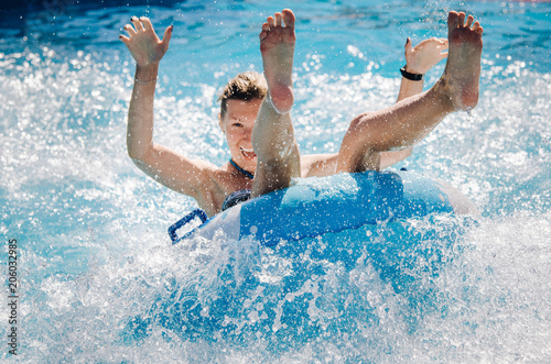 Funny girl taking a fast water ride on a float splashing water. Summer vacation with water park concept. photo