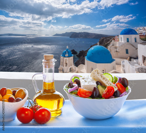 Greek salad against famous church in Oia village, Santorini island in Greece