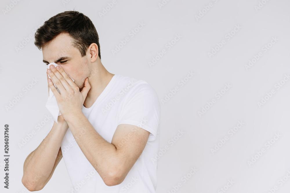 A young man sneezes into a napkin. Іsolated white background A young man sneezes into a napkin. Іsolated white background
