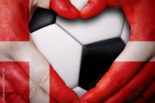 Hands painted with a Denmark flag forming a heart over soccer ball background