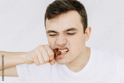 Close-up young man is eating a chocolate candy bar. Іsolated white background © Maksym