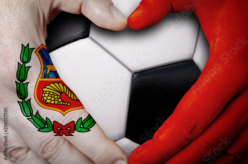 Hands painted with an Peru flag forming a heart over soccer ball background