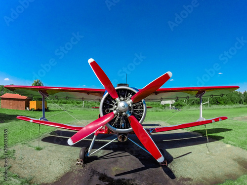 A small red sports red aircraft on a covered grass field in a sunny clear day.