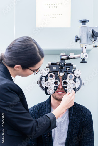 Optician and man at eye examination with phoropter in optician shop photo