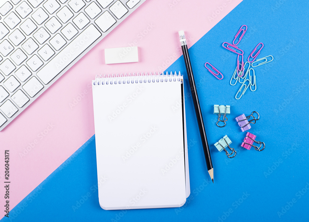 Computer keyboard next to notebook, pencil and stationery on pink and blue background. Back to school concept.