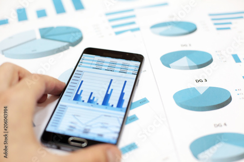 Businessman looks at business charts and graphs on paper and in smartphone