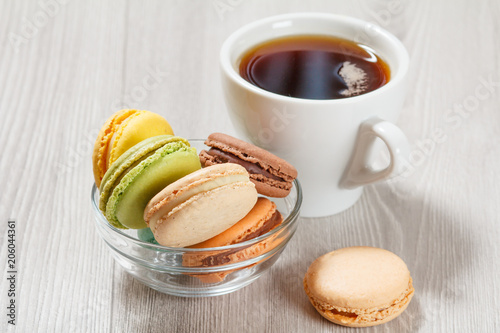 Tasty macaroons cakes of different color in glass bowl and cup of coffee