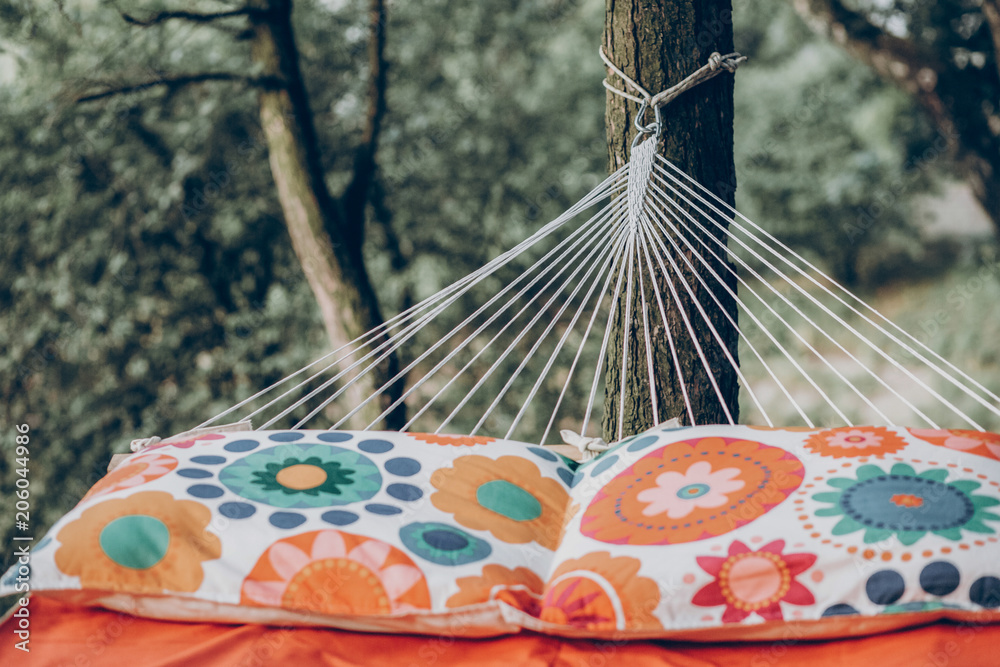 Obraz premium pillows on colorful stylish travel hammock in summer sunny park. resting, camping and relaxing outdoor, summer vacation and holiday. space for text. wanderlust and adventure