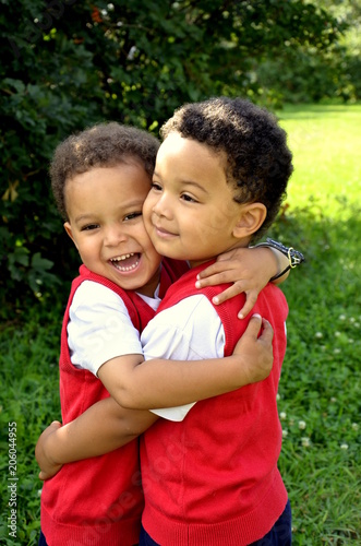 Cute mixed twins brothers hugging each other in the park. Beatiful handsome kids.