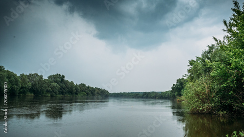 Rain and dramatic clouds over river and forest, panoramia