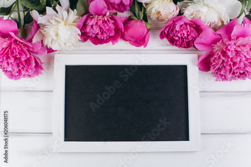 Pink and white peonies around blackboard on a wooden background. Copy space and flat lay.