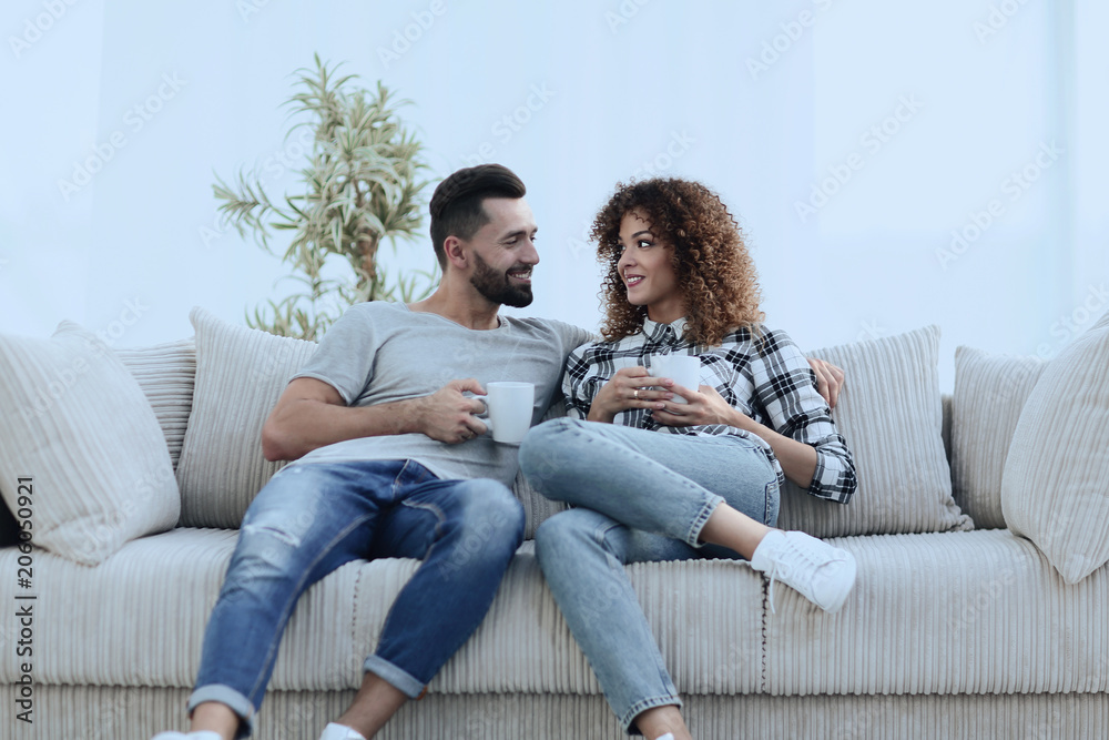 Beautiful couple holding a cup of drink while sitting on the couch at home Beautiful couple holding a cup of drink while sitting on the couch at home