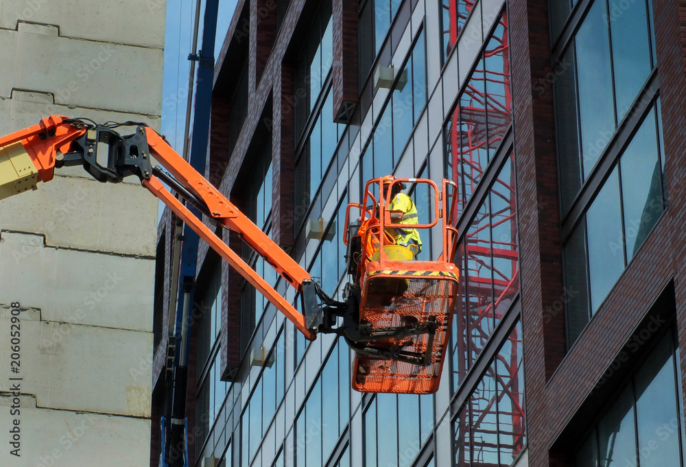 Fototapeta premium construction worker on an orange elevated platform on a large modern building site