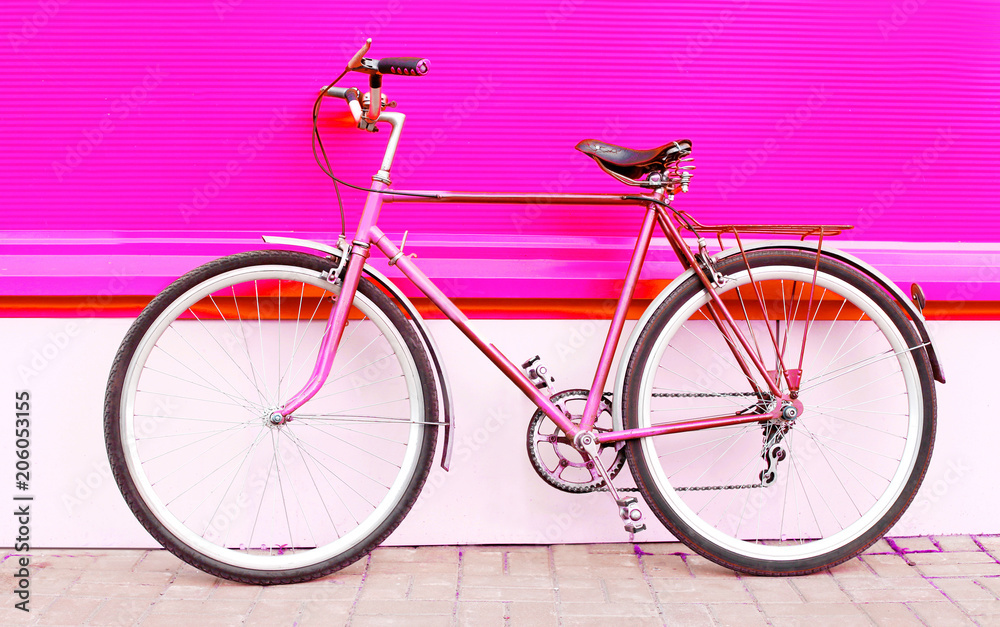 Retro pink bicycle stands over colorful pink background