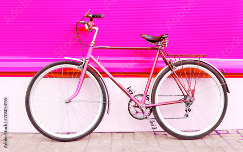 Retro pink bicycle stands over colorful pink background