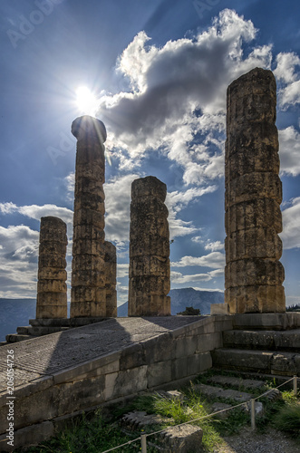 Delphi Town, Phocis - Greece. The Temple of Apollo (Olympian god of sun in ancient greek mythology) at the archaeological site of Delphi. Sun shines above the ancient columns of the temple. Cloudy sky