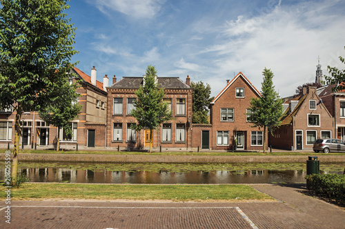Tree-lined canal with streets on the banks and brick houses on sunny day in Weesp. Quiet and pleasant village full of canals and green near Amsterdam. Northern Netherlands.