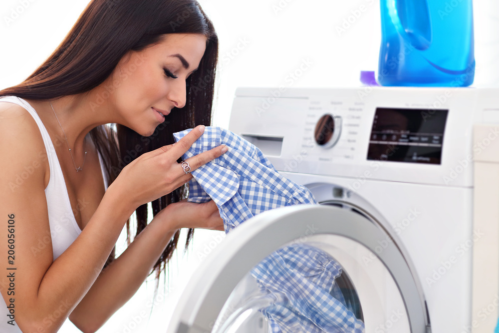 Portrait of young housewife with laundry next to washing machine