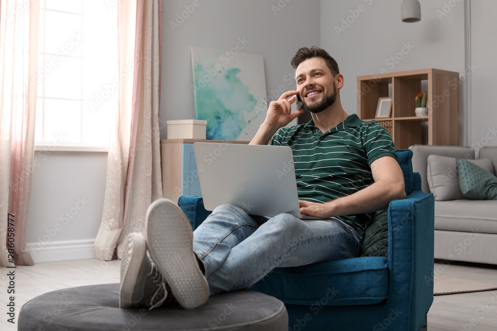 Young man working with laptop on armchair in home office