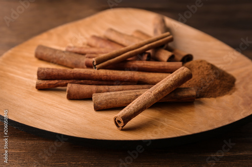 Plate with aromatic cinnamon powder and sticks on wooden table