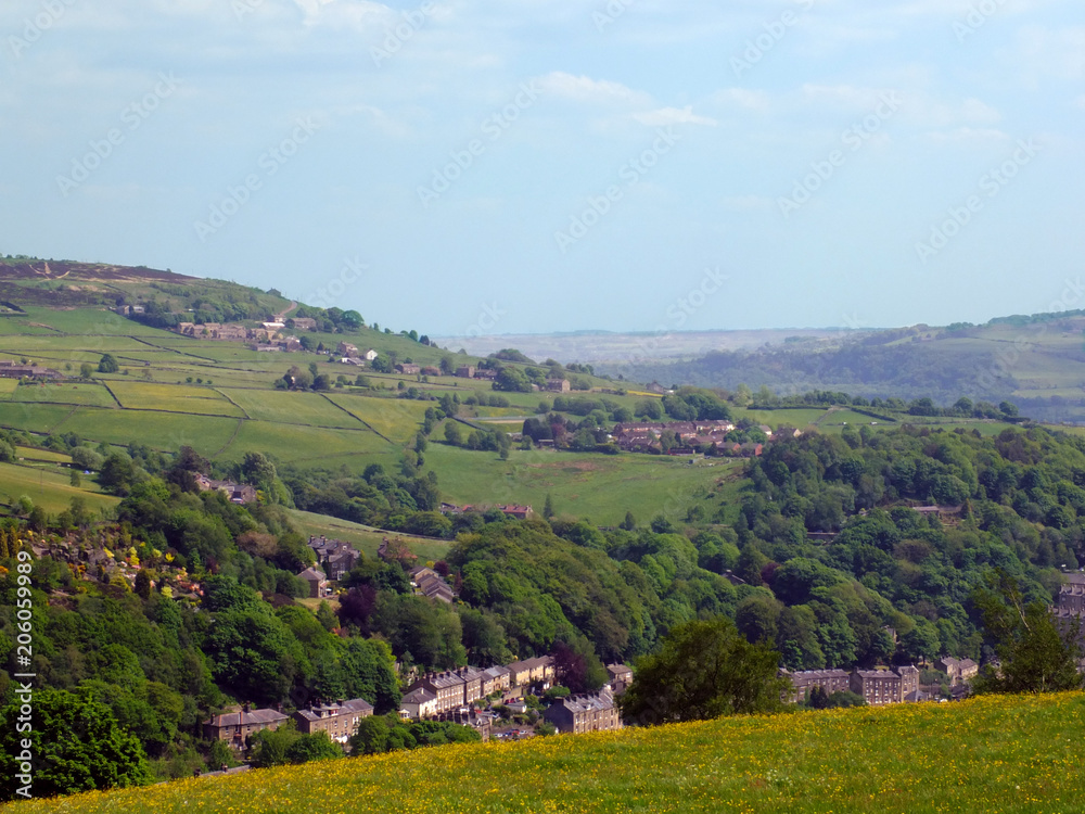 the town of hebden bridge visible at the bottom of the calder valley with surrounding pennine yorkshire countryside with fields woodland and hills in spring sunlight with bright blue sky