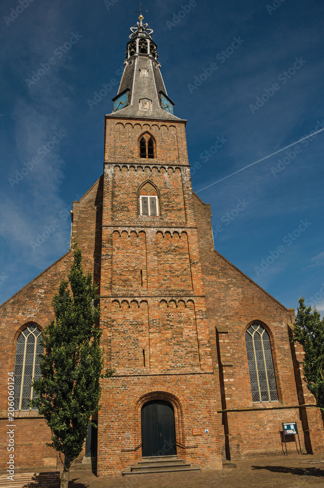 Steeple on the church facade made of bricks in front of a narrow street and sunny blue sky at Weesp. Quiet and pleasant village full of canals and green near Amsterdam. Northern Netherlands.