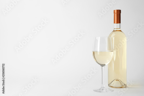 Bottle and glass of expensive white wine on light background