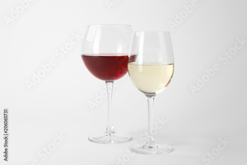 Glasses of expensive red and white wines on light background