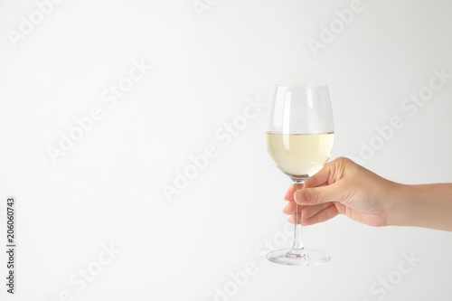 Woman holding glass of expensive white wine on light background