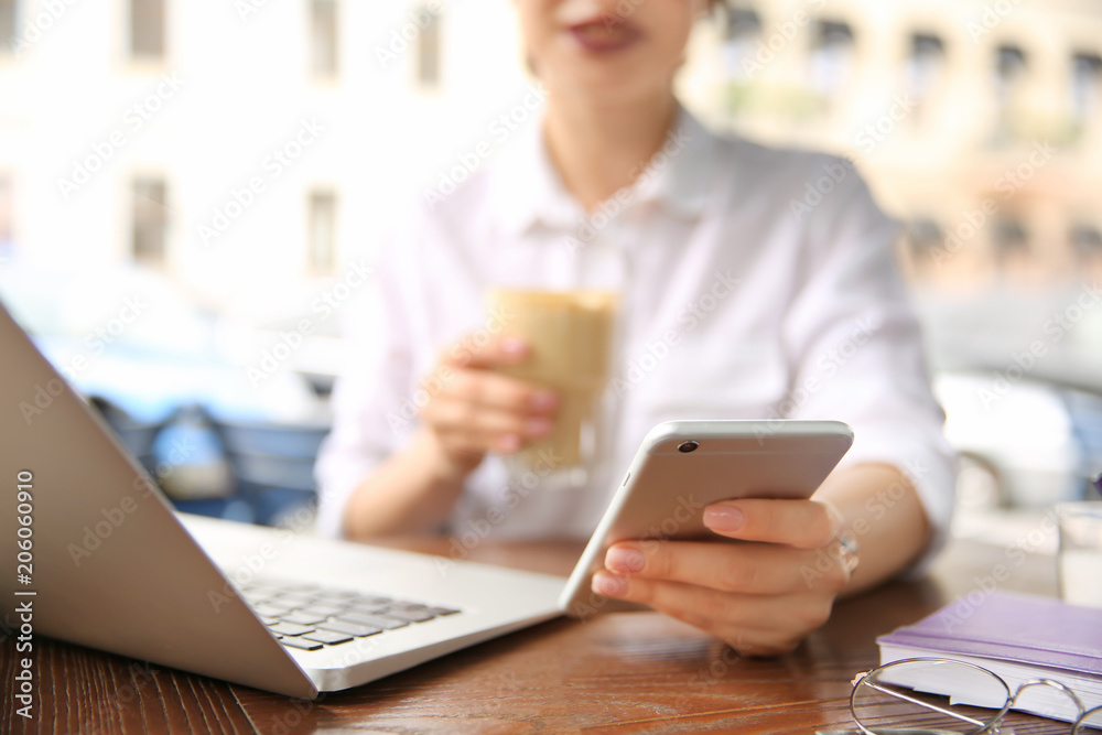 Young woman using mobile phone while working with laptop at desk, closeup Young woman using mobile phone while working with laptop at desk, closeup