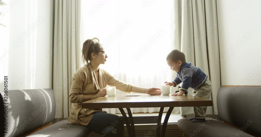 Toddler boy stands up and grabs coffee cup with mother - slow motion Toddler boy stands up and grabs coffee cup with mother - slow motion