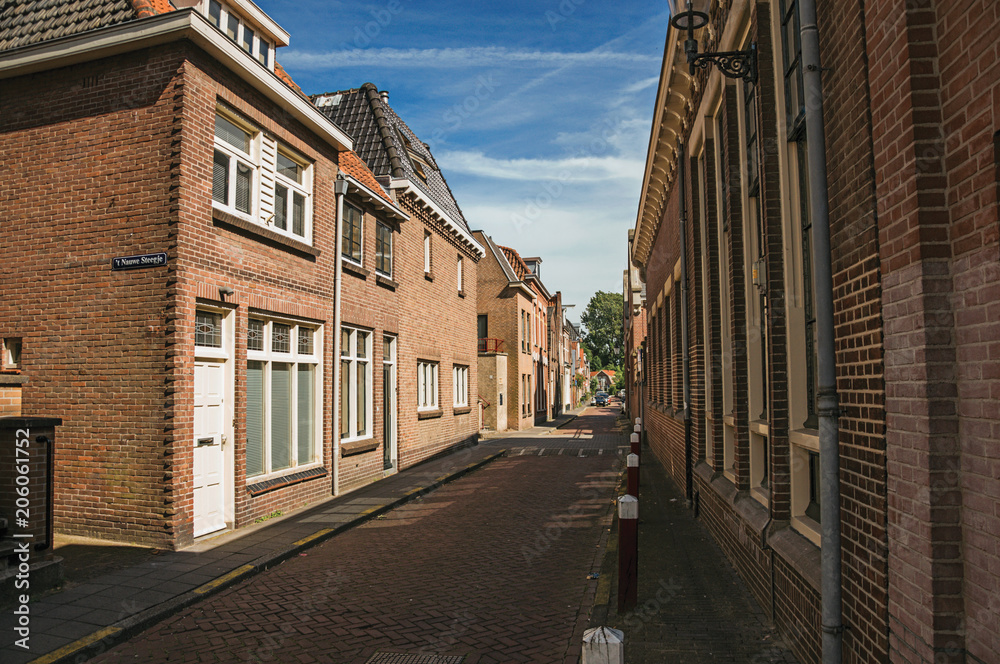 Working-class brick houses in a narrow empty street under sunny blue sky at Weesp. Quiet and pleasant village full of canals and green near Amsterdam. Northern Netherlands.