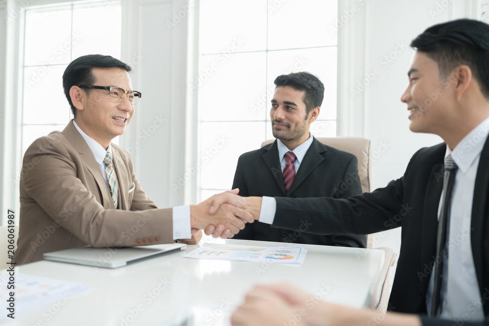 A confident business team of mixed ages and ethnicity making handshaking while meeting in a modern office. They are discussing ideas for their business development. A confident business team of mixed ages and ethnicity making handshaking while meeting in a modern office. They are discussing ideas for their business development.