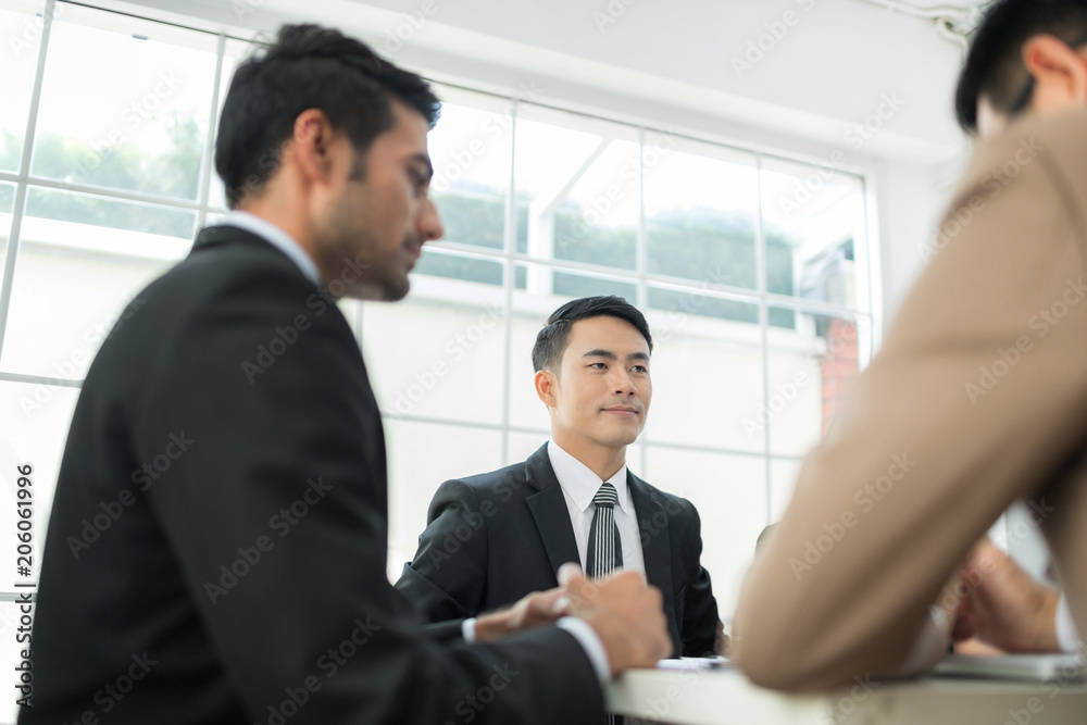 A confident business team of mixed ages and ethnicity are holding a meeting in a modern office. They are discussing ideas for their business development.