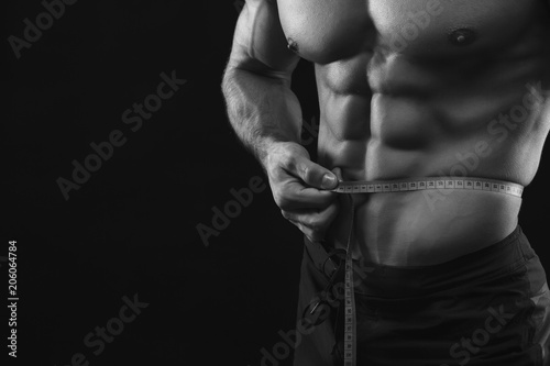 Unrecognizable muscular man measuring waist