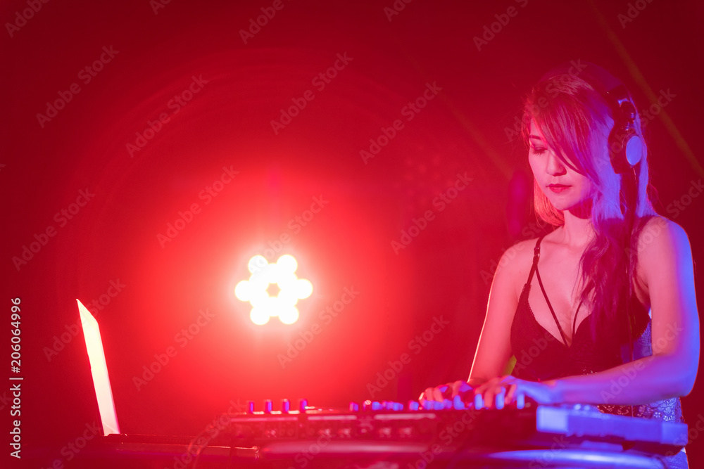 Portrait of active pretty young DJ woman playing music on laser lighting background.