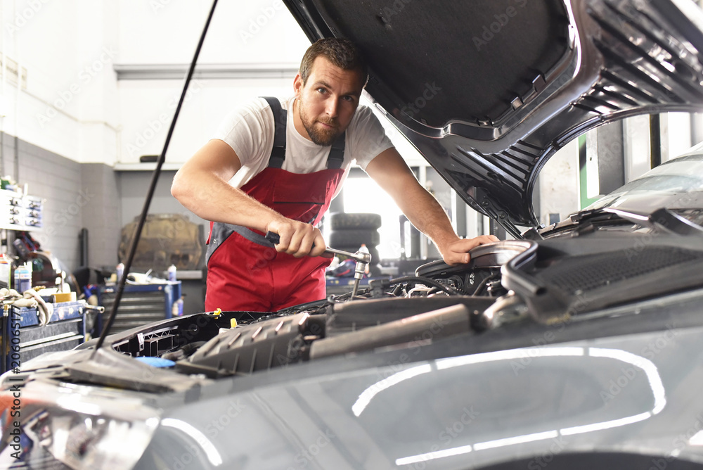 Portrait KFZ-Mechaniker repariert Auto in einer Werkstatt // Car mechanic  repairs car in a workshop Stock-Foto