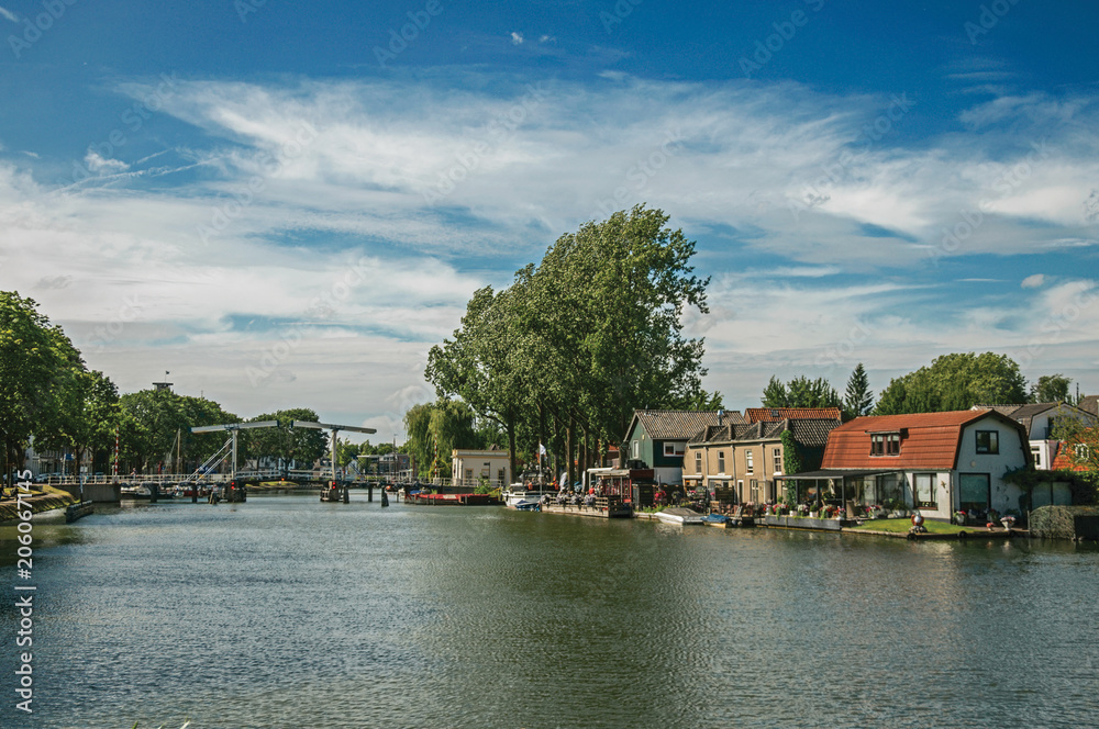 Vecht River with bridge, boats on the banks and brick houses on a sunny day in Weesp. Quiet and pleasant village full of canals and green near Amsterdam. Northern Netherlands.