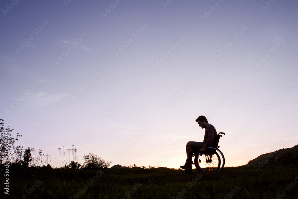 A young man in wheelchair in nature in the evening.