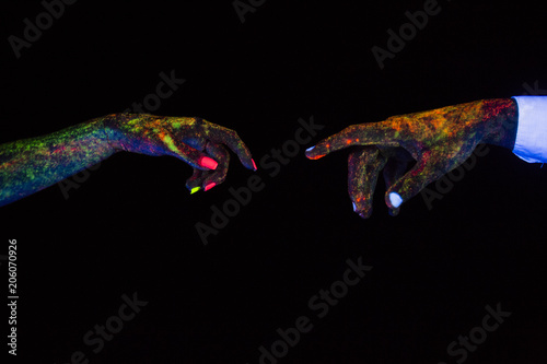 concept of connecting hands creative shooting in neon light male and female palms together stretch towards each other glow in the dark under ultraviolet