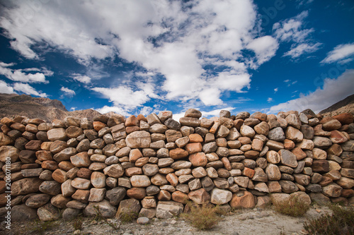 The stone wall constructed from the different sizes the boulders in grey, brown, tawny tints. Bright blue sky with white clouds. Ideal background for the illustrations and collages.